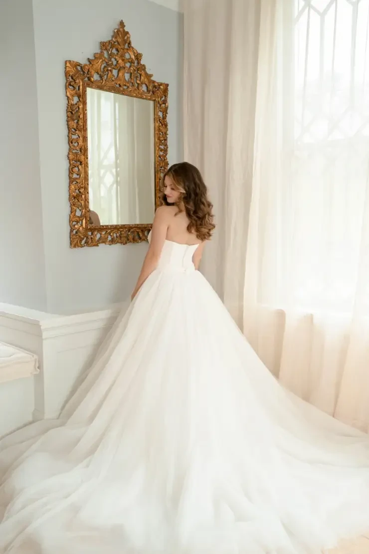 Model is wearing a strapless ball gown wedding dress with boning on the bodice