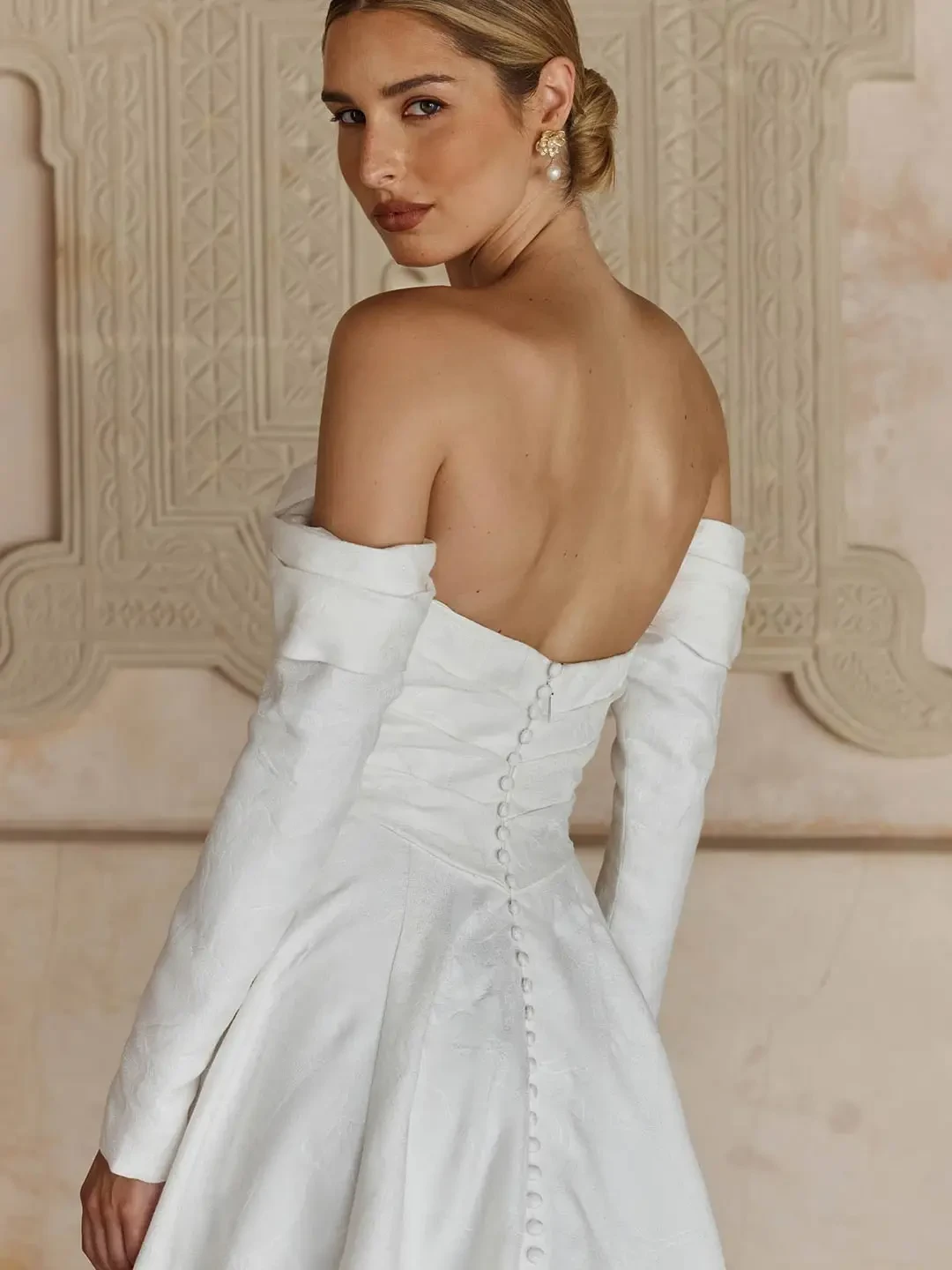 Model is wearing a strapless ivory brocade A-line gown with a sweetheart neckline, Basque waist, and optional statement sleeves and bow.