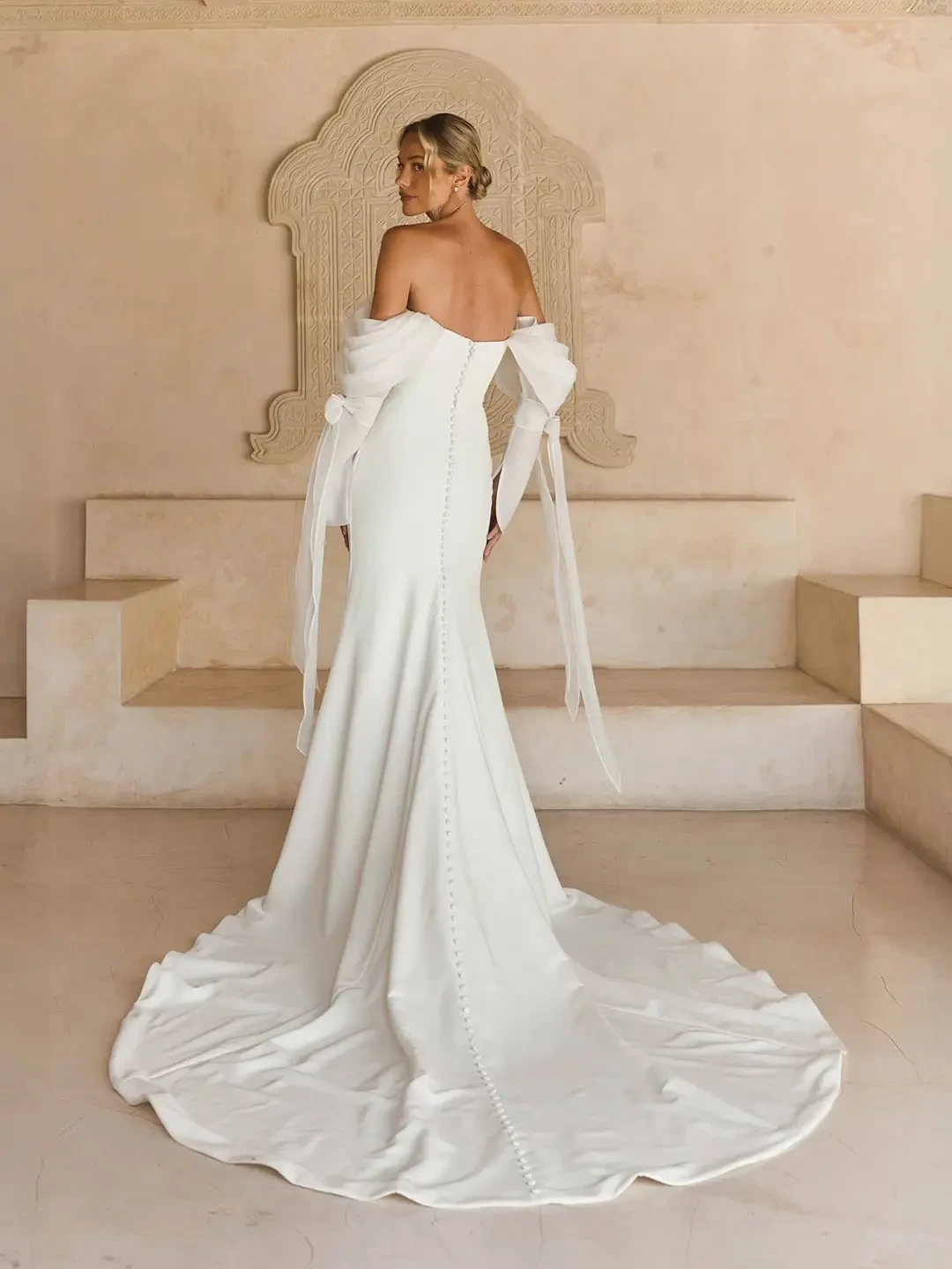 Model is wearing a fitted strapless crepe gown with asymmetric pleating, a sweetheart neckline, leg slit, and detachable pleated organza sleeves.