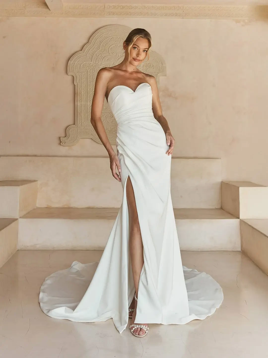 Model is wearing a fitted strapless crepe gown with asymmetric pleating, a sweetheart neckline, leg slit, and detachable pleated organza sleeves.