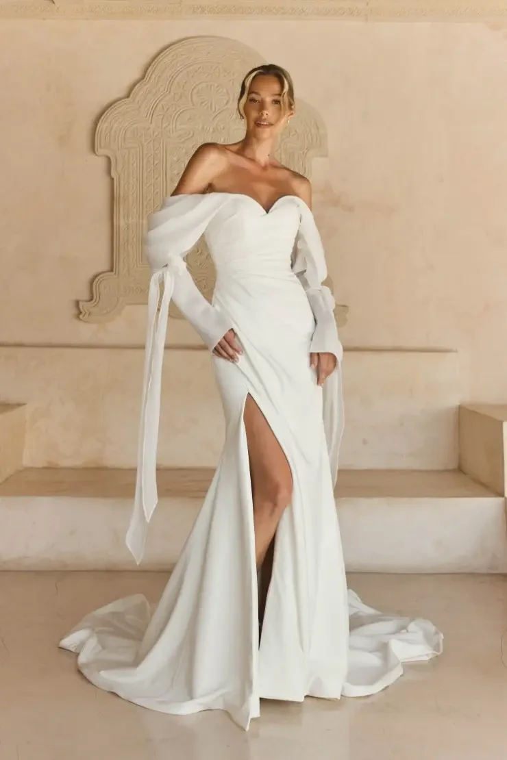 Model is wearing a crepe sheath wedding dress with detachable organza sleeves