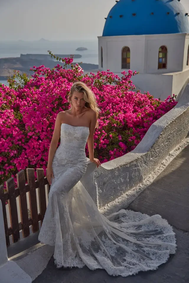 Model is wearing a strapless sheath bridal dress with lace appliques