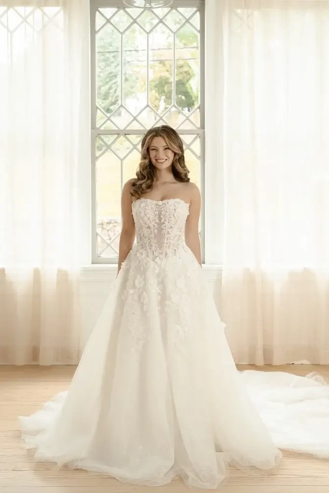 Model is wearing a tulle strapless bridal gown with 3d floral appliques 