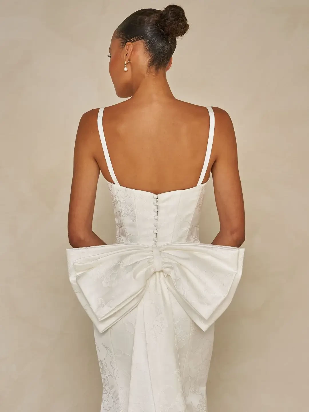 Model is wearing a floral jacquard sheath gown with a square neckline, detachable straps, an overskirt for added volume, and an optional back bow.