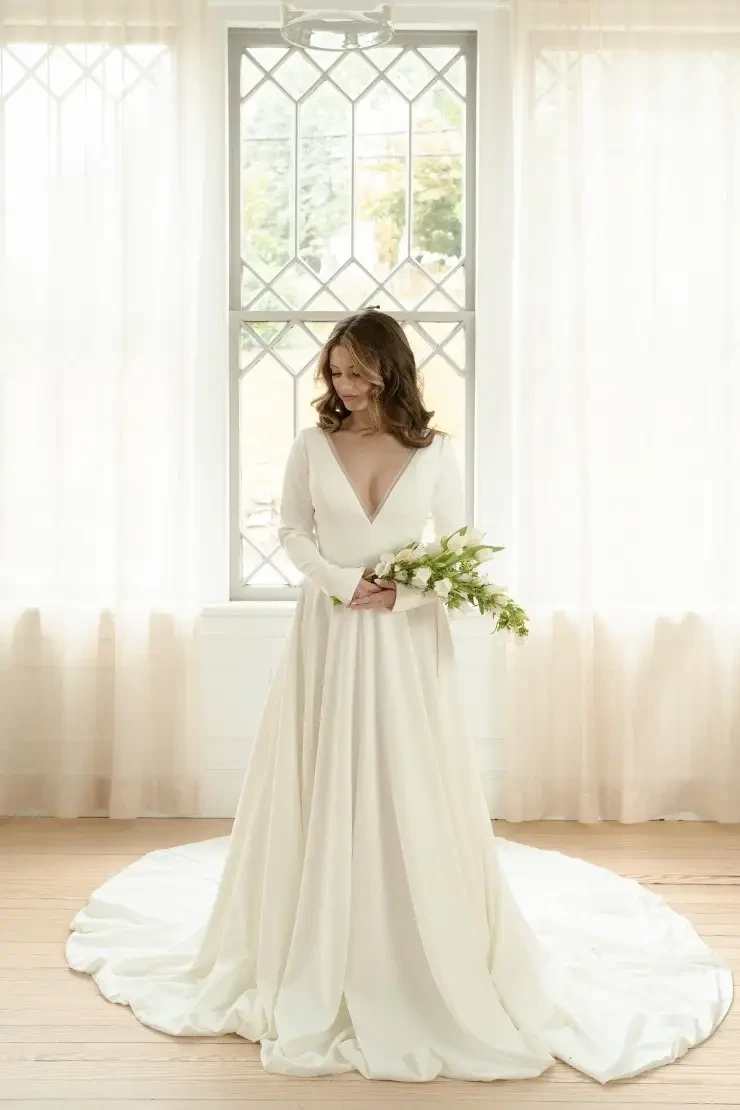 Model is wearing a long sleeve a-line wedding dress with a plunging neckline