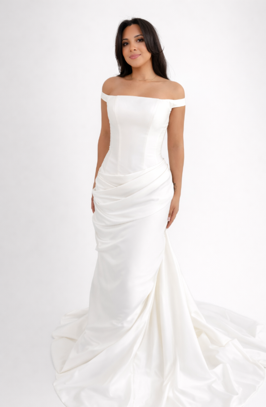 A woman wearing an off-the-shoulder white wedding dress, standing against a plain background.
