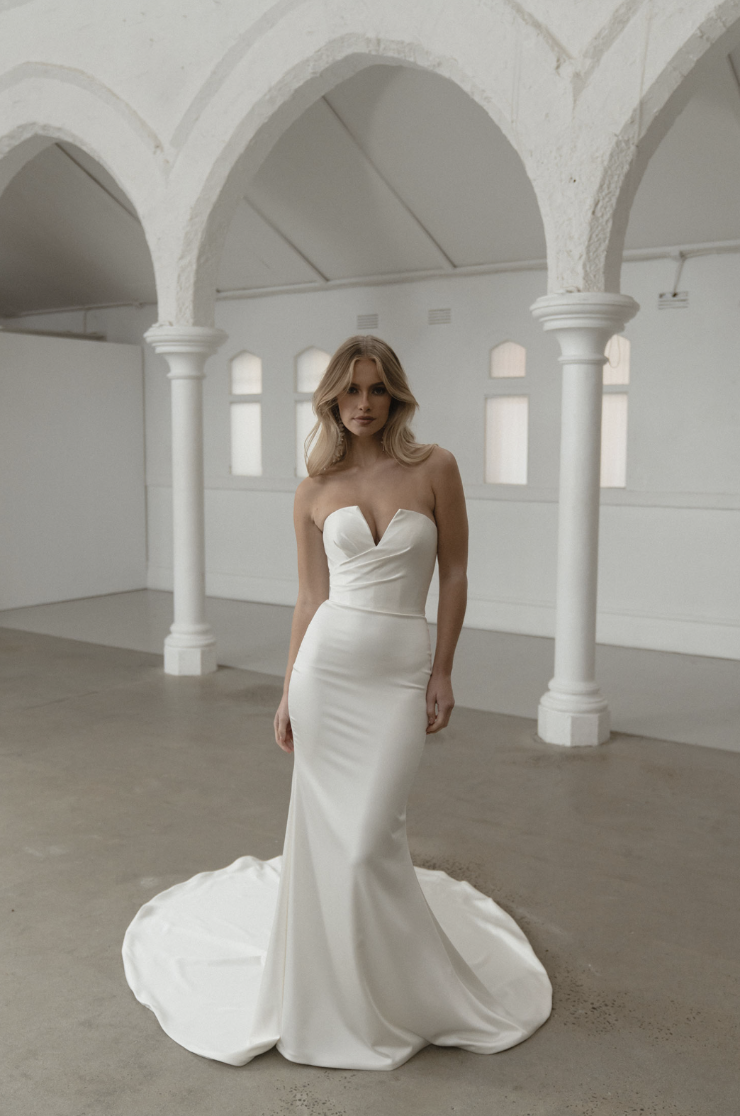 model is wearing a strapless fit and flare bridal gown with a bow on the back