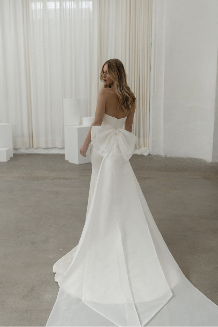 model is wearing a strapless fit and flare bridal gown with a bow on the back